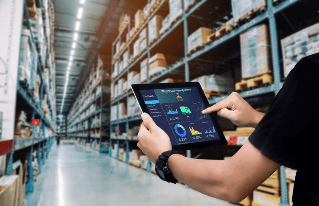 Almacén logístico donde una persona esta controlando las mercancías mediante una tablet electrónica.