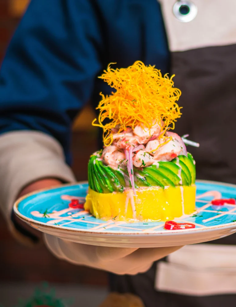 Plato gastronómico presentado con aguacate, marisco y crujiente sobre una vajilla azul